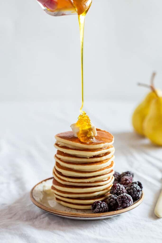 stack of pancakes on a white plate with syrup being drizzled on top