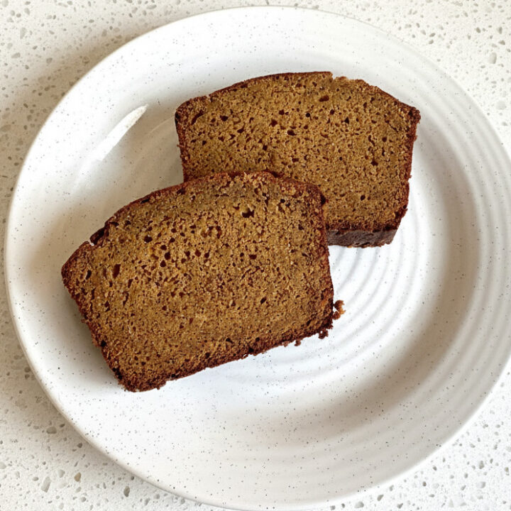 2 slices of apple cider pumpkin bread on a white plant sitting on a white granite countertop
