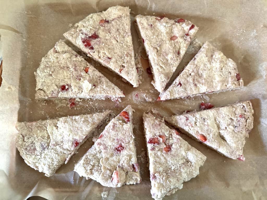 Uncooked strawberry buttermilk scone dough rolled in a circle and cut into 8 wedges that have been slightly separated on a piece of parchment paper