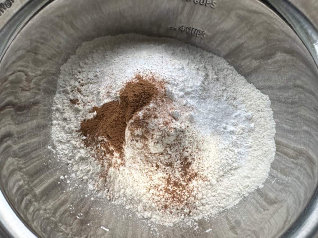 Flour, sugar, cinnamon, and baking powder measured out in a stainless steel bowl