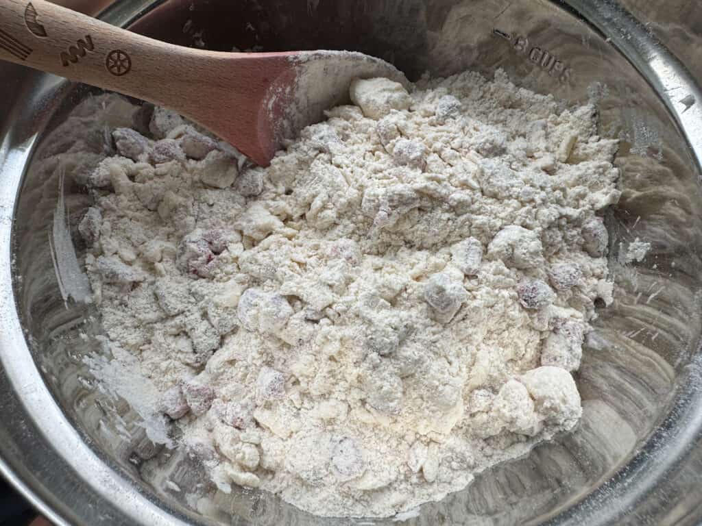 Dry ingredients, butter, and strawberries mixed together in a stainless steel bowl