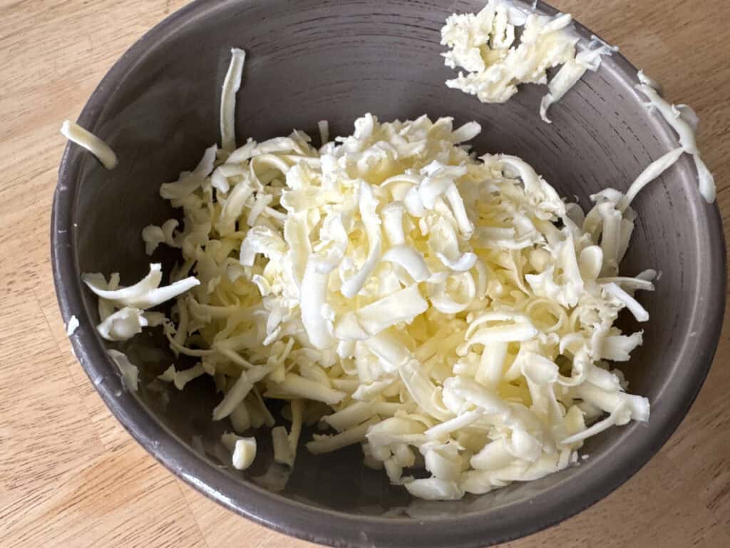 Grated butter in a gray bowl on a light wooden table