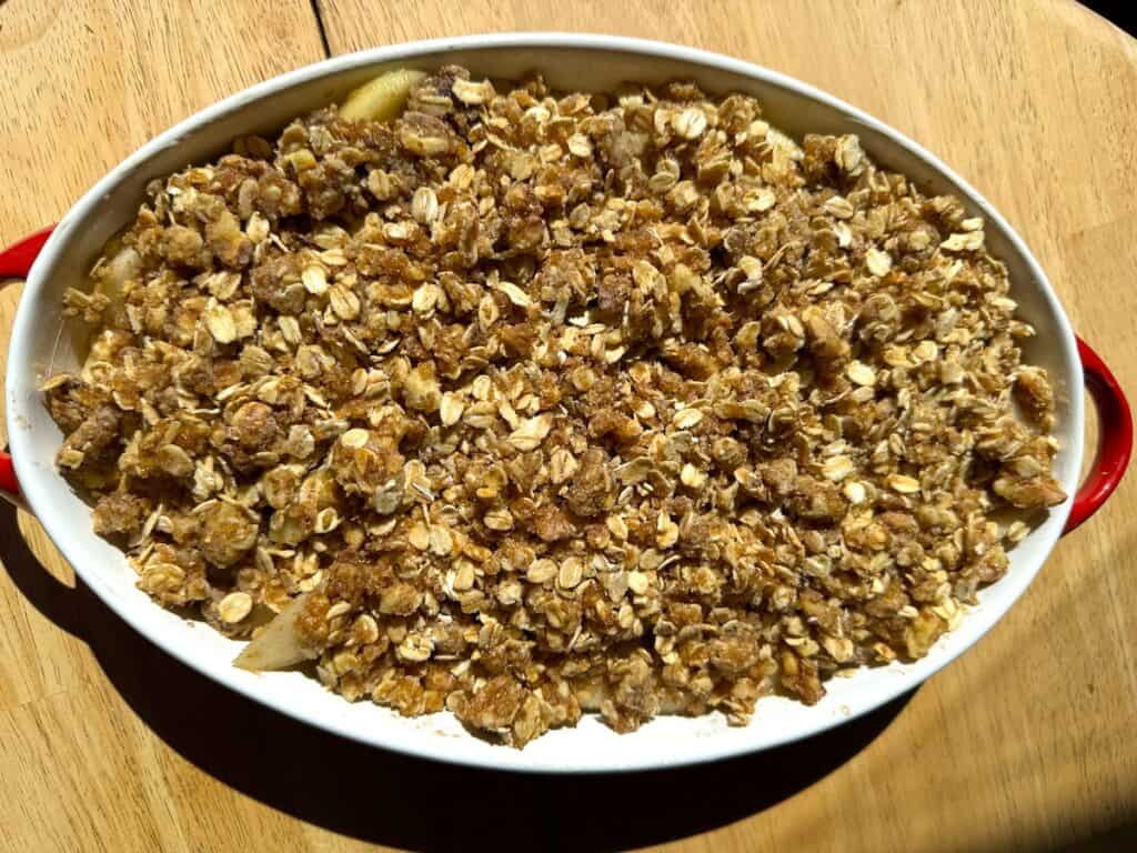 brown butter honey pear crisp with topping ready to bake in a red and white baking dish on a wooden table
