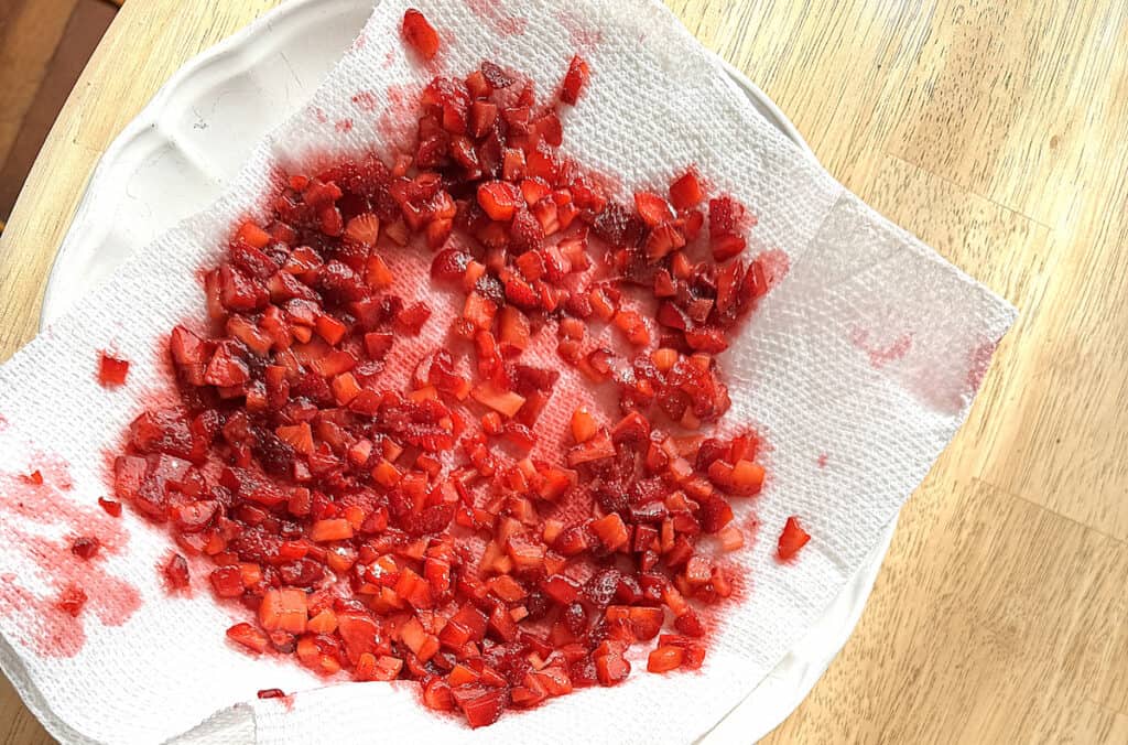 diced strawberries on a paper towel that's covering a white plate on a light wooden table