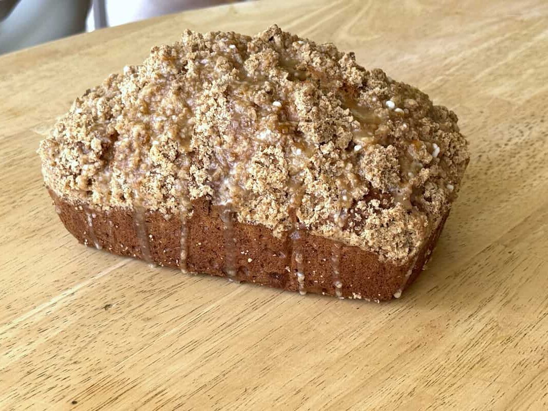 peach butter quick bread with streusel topping and peach butter glaze on a wooden table.