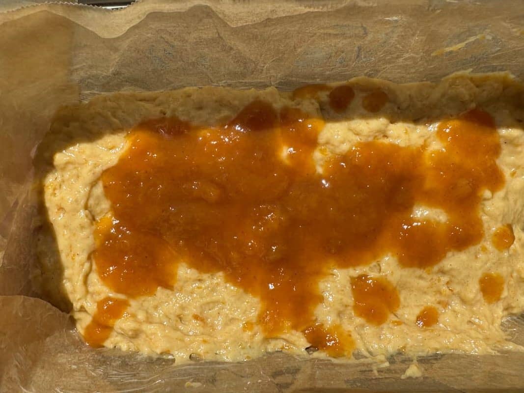 half of the peach butter quick bread batter in a parchment lined pan with peach butter drizzled on top