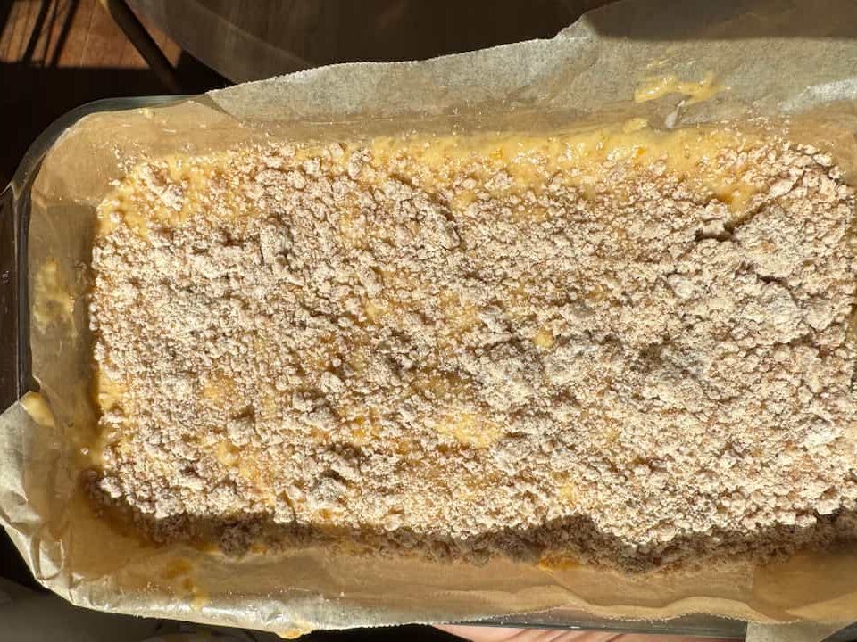 peach butter bread batter in a parchment lined pan with streusel topping sprinkled on top