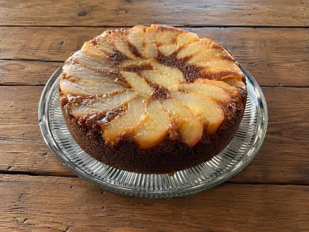 pear upside down cake on a glass plate sitting on a wooden table
