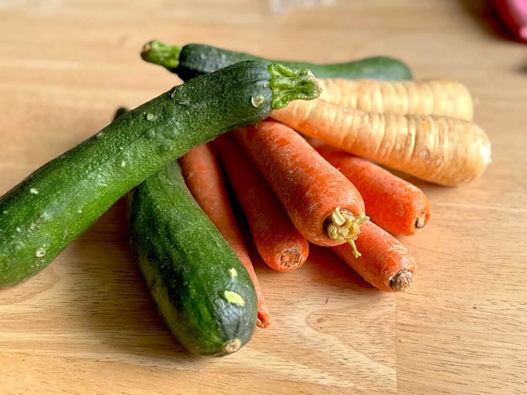 3 zucchini, 5 carrots, and 2 parsnips stacked in a pile on a light wooden table