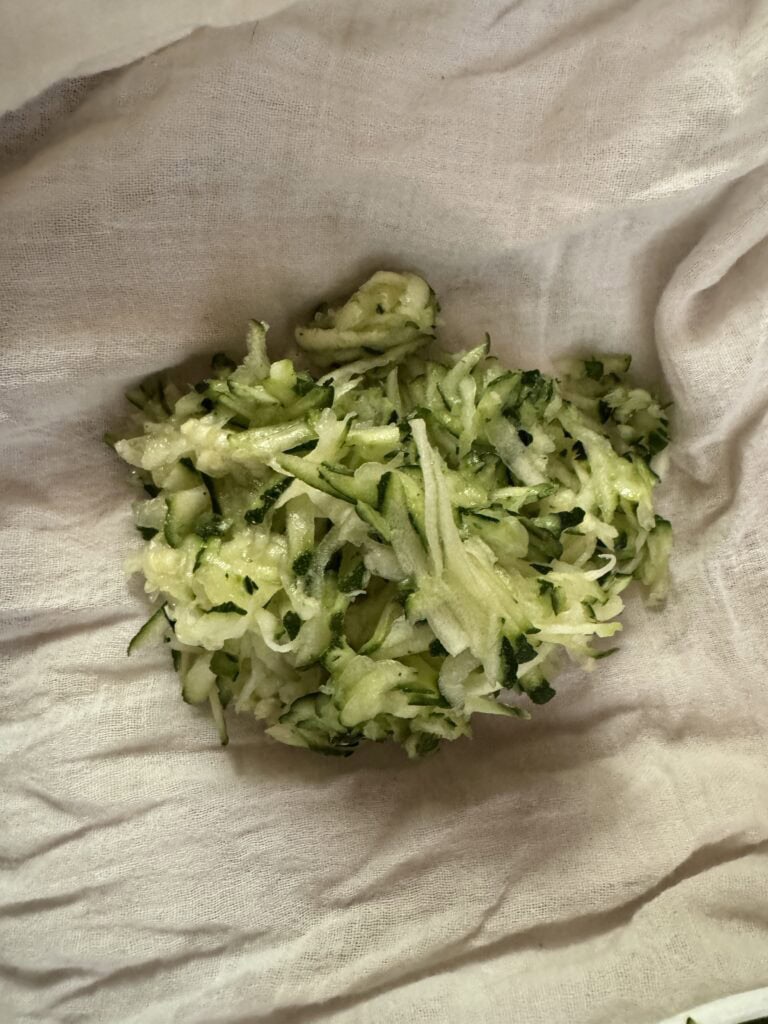 Shredded zucchini in a white flour sack kitchen towel