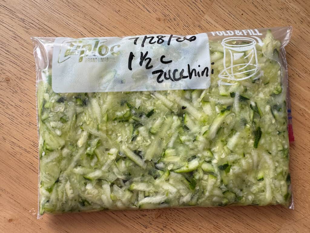 1 1/2 cups of shredded zucchini in a ziploc bag flattened on a wooden table ready to go into the freezer