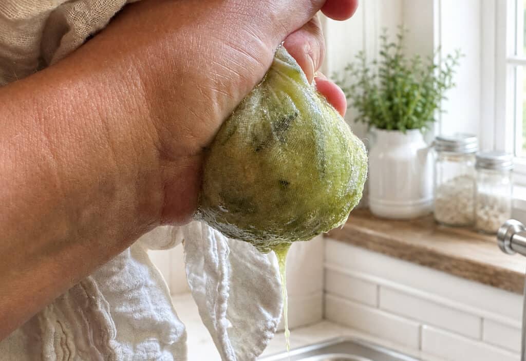 hand holding a kitchen towel with zucchini in it squeezing the water out of it.