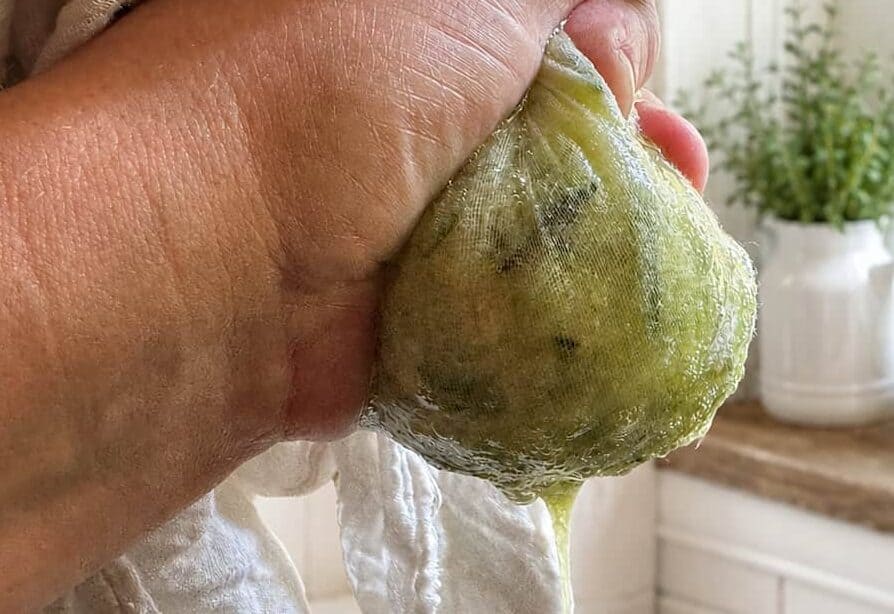 hand holding a kitchen towel with zucchini in it squeezing the water out of it.
