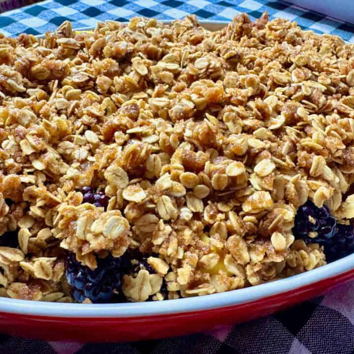 baked apple blackberry crisp in a red baking dish on a black and white checkered table cloth