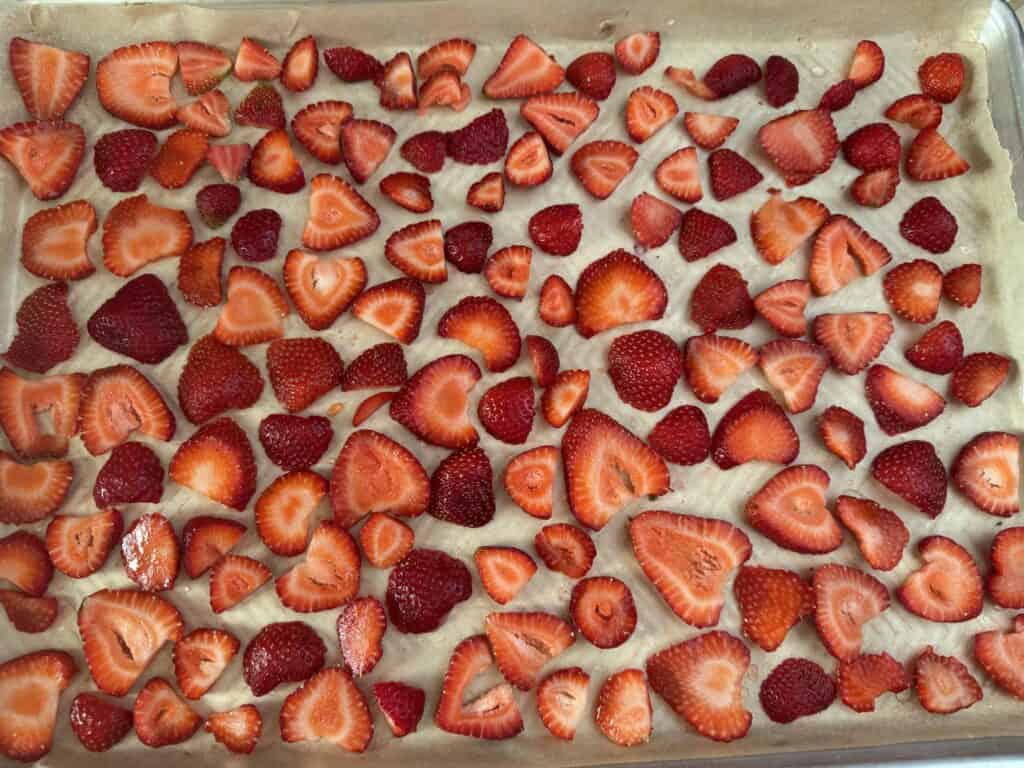 a single layer of sliced strawberries on a parchment lined tray
